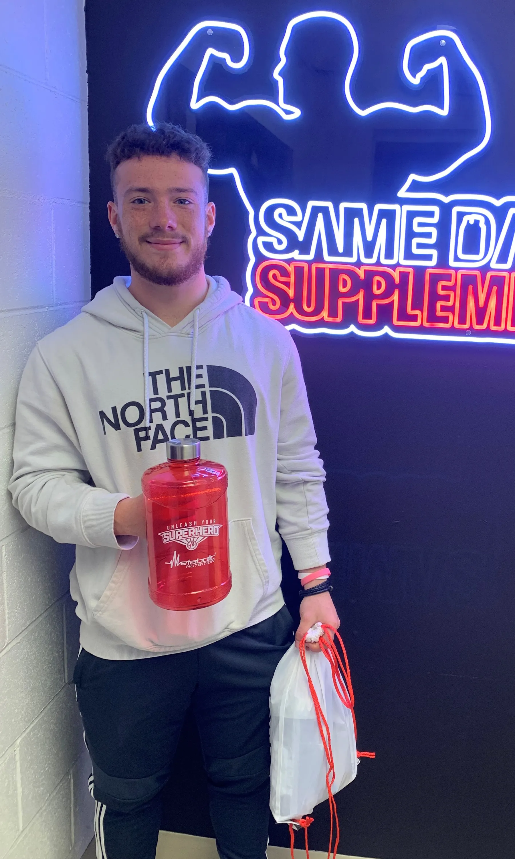 Customer holding red Metabolic Nutrition water jug and SameDaySupplements drawstring bag